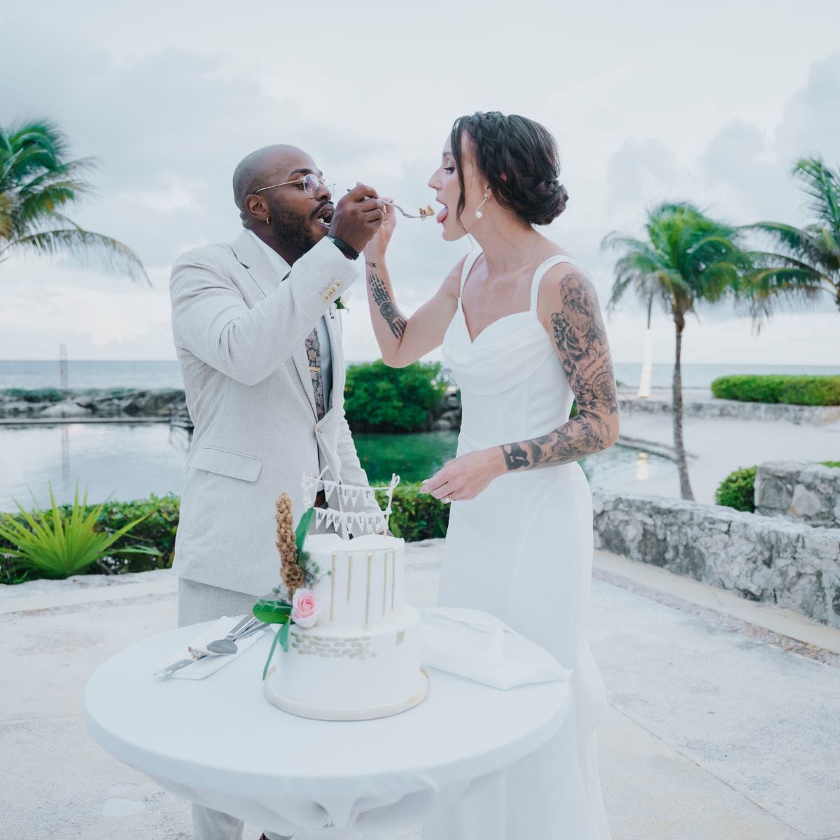 Madison and Blake enjoy cake outdoors in wedding attire at their destination wedding by water.