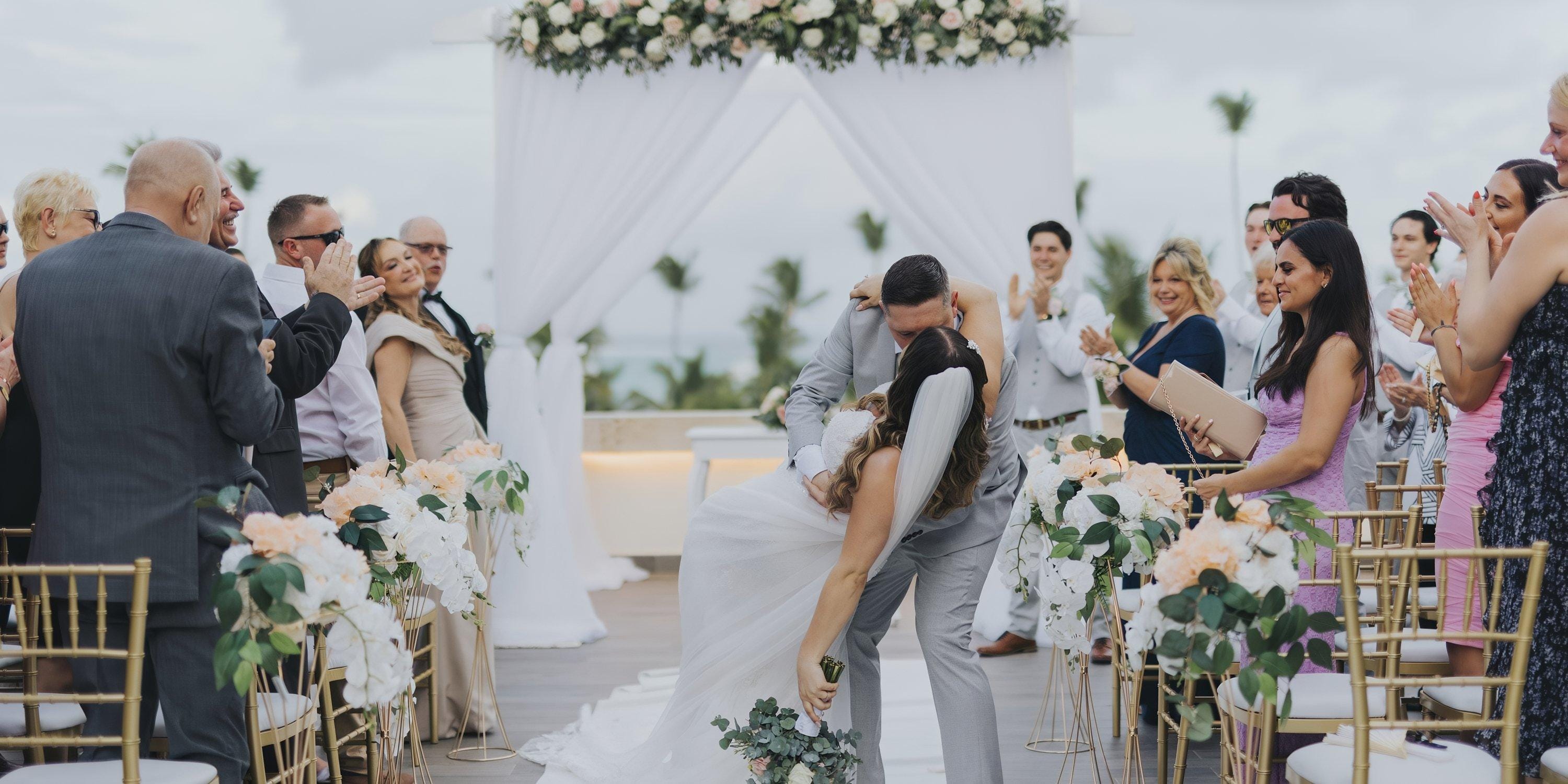 The bride and groom kiss at their destination wedding at Lopesan Costa Bavaro as guests applaud outdoors.
