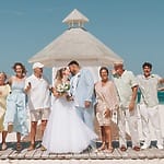 A destination wedding party celebrates on a beach boardwalk in front of a gazebo.