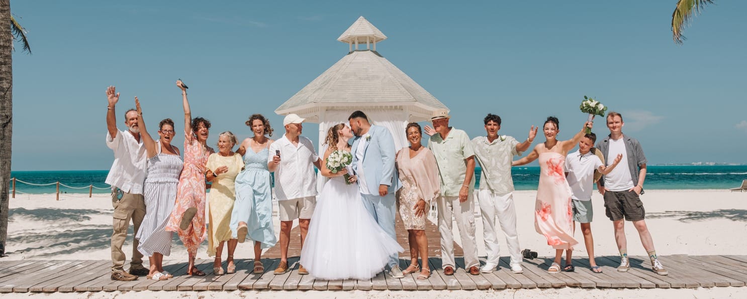 A destination wedding party celebrates on a beach boardwalk in front of a gazebo.